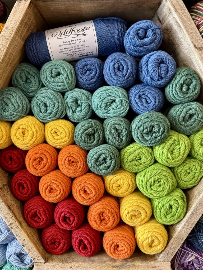 A variety of colorful yarn skeins organized in a hexagonal wooden basket, featuring shades of blue, green, yellow, orange, and red.